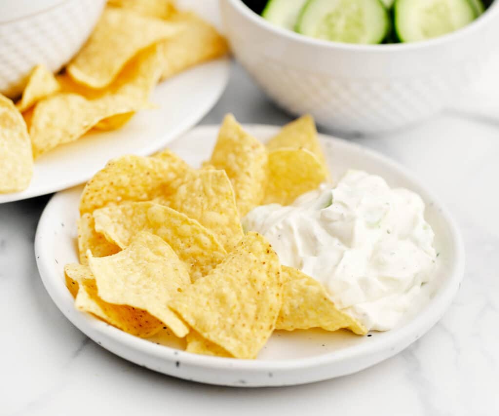Cucumber Dip on Plate with Tortilla Chips and Bowl of Cucumbers in the Background