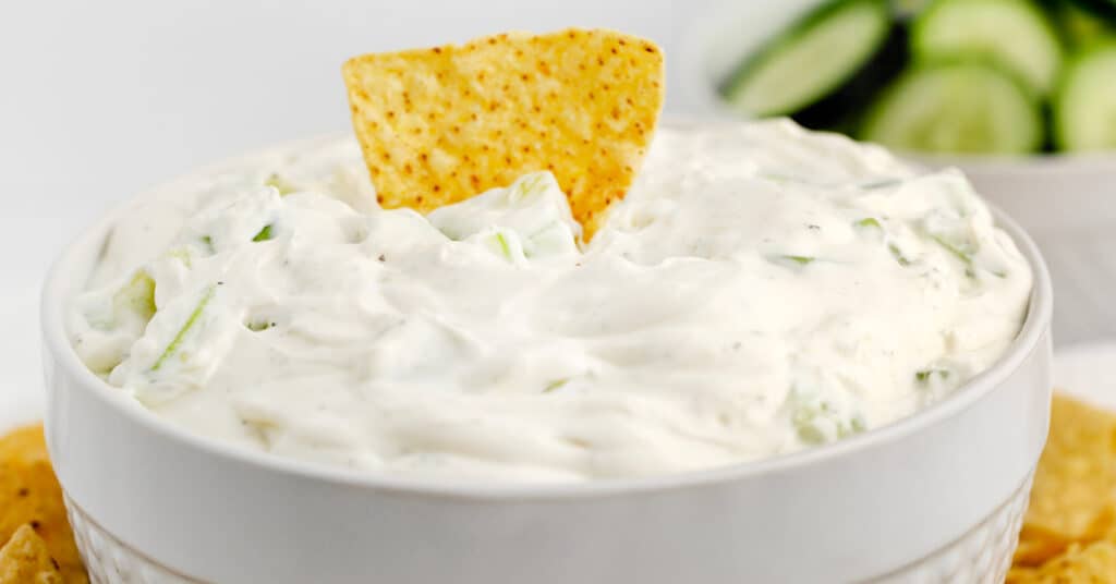 Cucumber Dip in Bowl with Chip and Cucumbers in the Background
