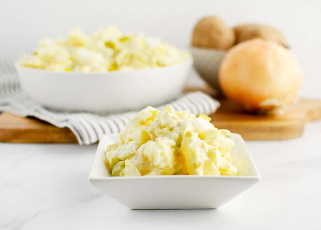 Potato Salad in Square Bowl with Large Bowl of Potato Salad and Fresh Potatoes and Onions in the Background