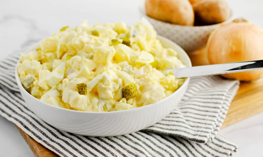 Potato Salad in White Bowl with Spoon on Kitchen Towel