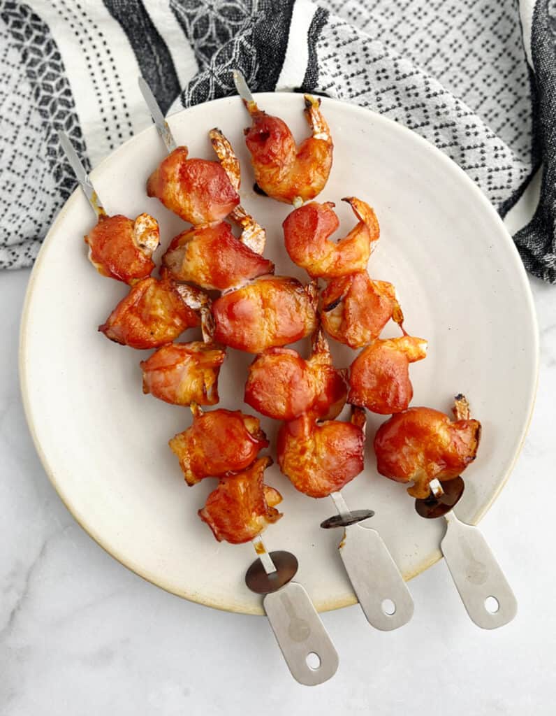 Bacon Wrapped Shrimp Skewers on Plate with Kitchen Towel in the Background