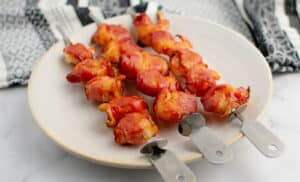 Bacon Wrapped Shrimp Skewers on Plate with Kitchen Towel in the Background