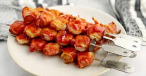 Bacon Wrapped Shrimp Skewers on Plate with Kitchen Towel in the Background