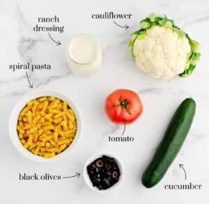 Spiral Pasta, Tomato, Cucumber, Head of Cauliflower, Olives, and Ranch on White Marble Counter
