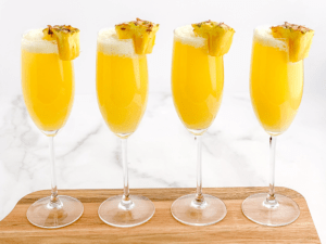 Pineapple mimosas in a line on a wood serving tray