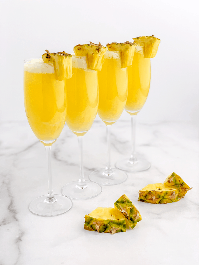 Pineapple mimosas in a line with pineapple garnishes