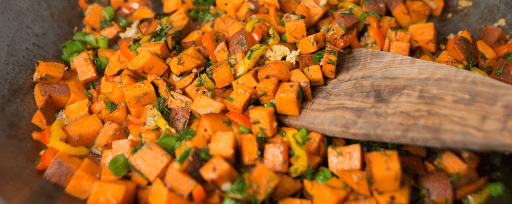 Sweet Potato Hash Topped with Fresh Herbs Being Stirred with a Wooden Spoon