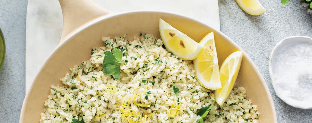 Cauliflower Rice in a Bowl Garnished with Lemon Wedges