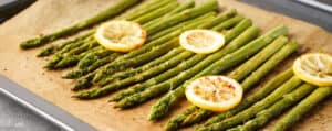 Cooked Asparagus Topped with Lemon Slices on a Baking Sheet with Parchment Paper