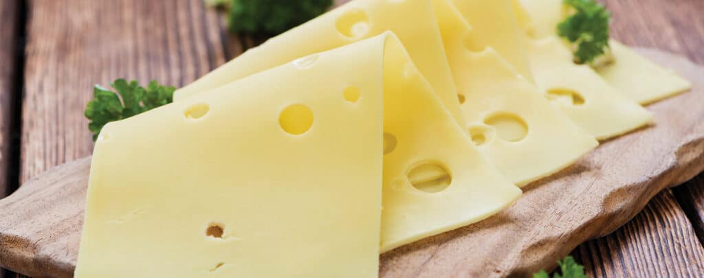 Swiss Cheese Slices on a Wooden Cutting Board and Table Garnished with Fresh Herbs