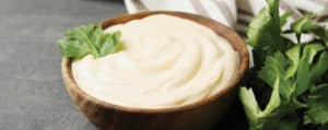 Mayonnaise in a Wooden Bowl Garnish with Fresh Herbs on a Dark Grey Countertop