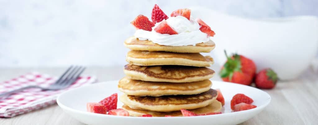 Stack of Pancakes Topped with Sliced Strawberries and Whipped Cream