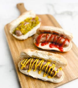 Brats on a Wooden Cutting Board Topped with Mustard, Ketchup, and Relish