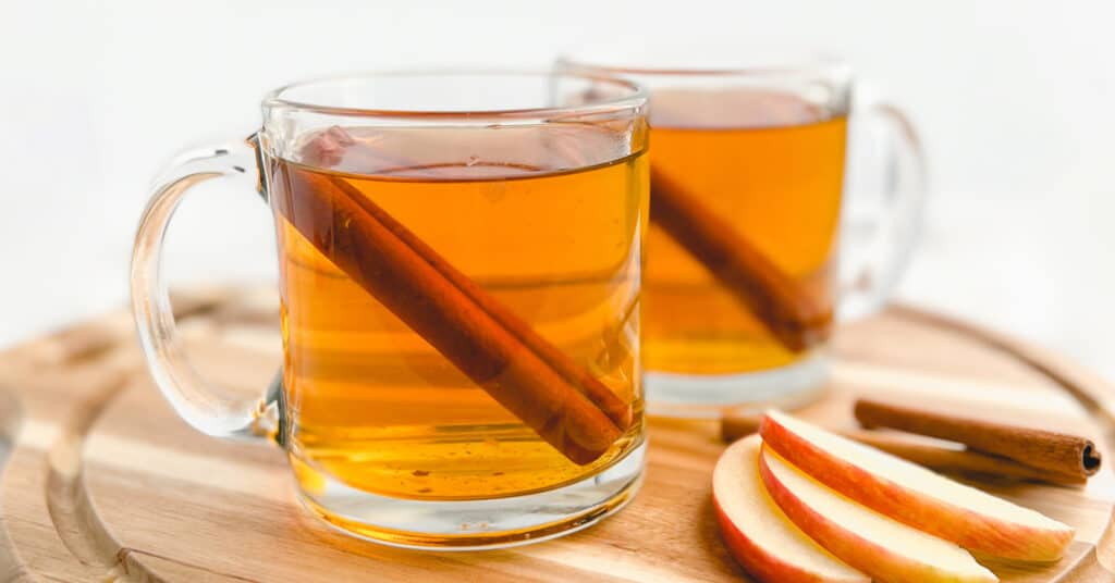 Hot Apple Cider in Glass Mugs with Cinnamon Sticks and Apple Slices on a Wooden Cutting Board