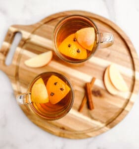 Hot Apple Cider in Mugs with Oranges, Cloves, Cinnamon Sticks, Apples on Wooden Tray