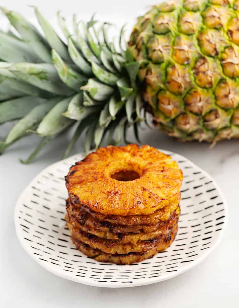 Air Fried Pineapple Rings on a Decorative Plate with a Fresh Pineapple Behind It