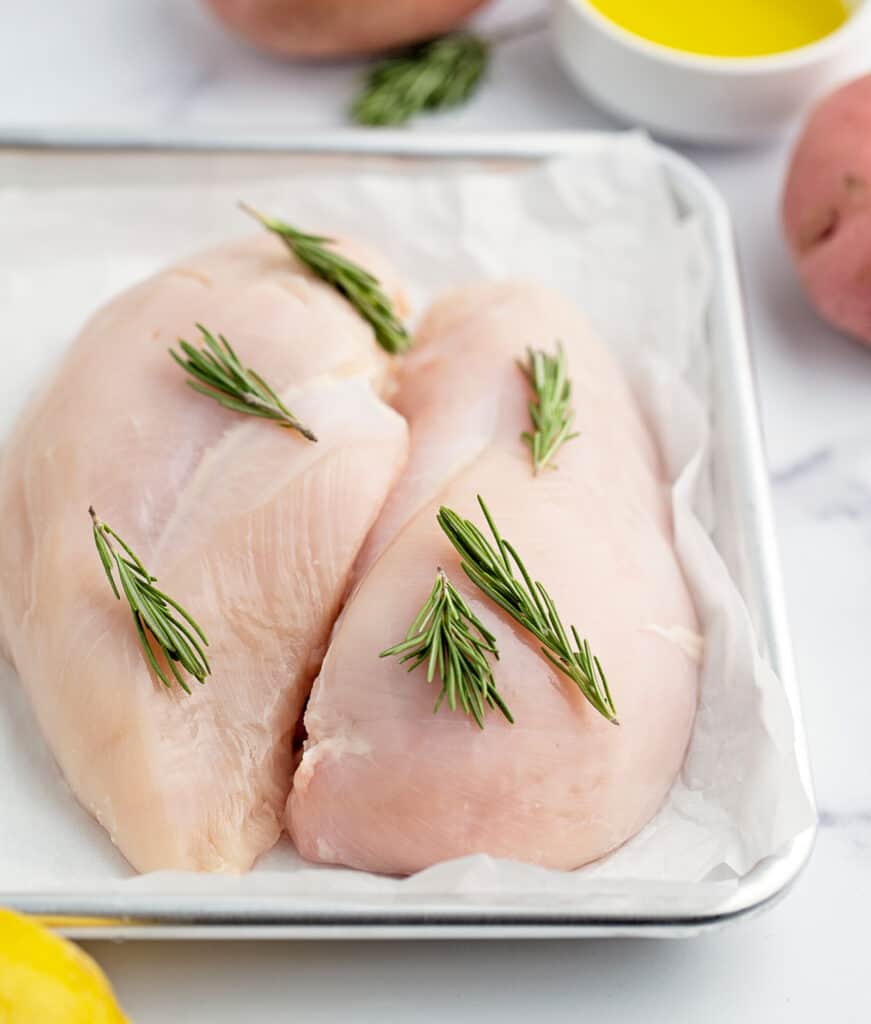 Raw Chicken on Baking Sheet Lined with Parchment Paper and Topped with Rosemary