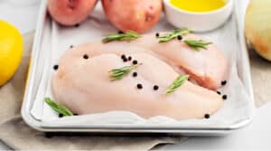 Raw Chicken on Baking Sheet Lined with Parchment and Topped with Peppercorns and Rosemary
