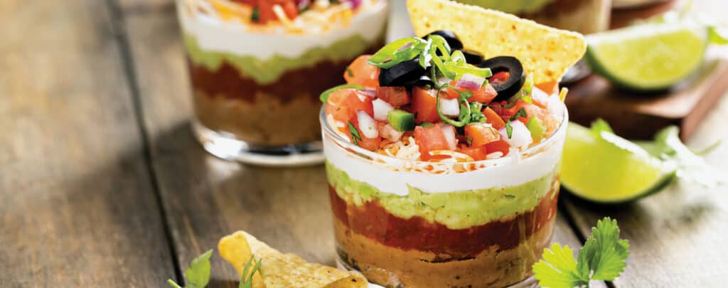 Cups of Seven Layer Dip with Lime Wedges and Tortilla Chips