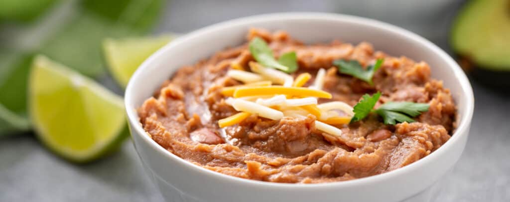 Bowl of Refried Beans Topped with Shredded Cheese with Lime Wedges on the Side