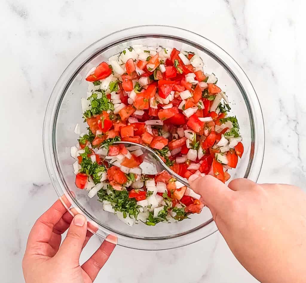 Stirring Pico de Gallo in Glass Bowl with Spoon