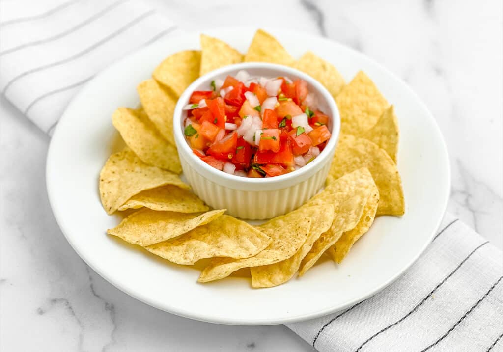 Fresh Pico de Gallo in Bowl with Circle of Tortilla Chips Around It on White Napkin with Black Stripes