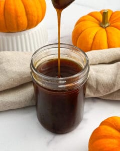 Pumpkin Spice Syrup Dripping Into Jar with Towels and Mini Pumpkins Around