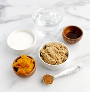 Sugar, Brown Sugar, Water, Pumpkin Puree, Vanilla, and Pumpkin Spice in Bowls on White Marble Surface