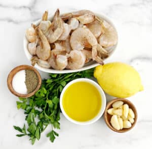 Raw Shrimp, Salt, Pepper, Olive Oil, Lemon, Parsley and Garlic on White Surface