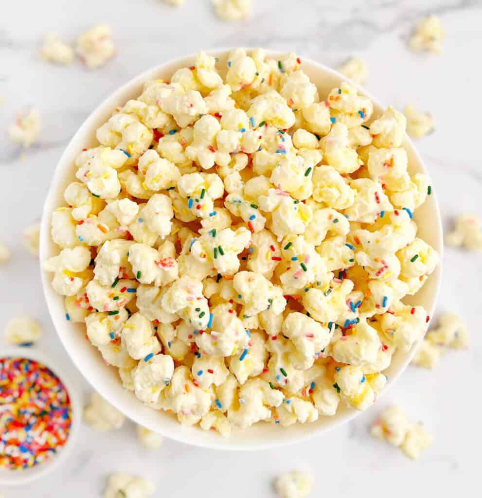 Top View of White Chocolate Puffcorn in Large Serving Bowl with Small Bowl of Sprinkles Beside It