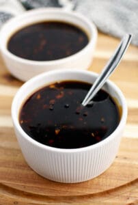 Homemade Teriyaki Sauce in Serving Bowls with Spoon on Wooden Surface with Kitchen Towel in Background