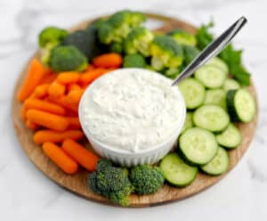 Green Goddess Dip in a Bowl with Spoon and Veggies Surrounding on a Wooden Cutting Board