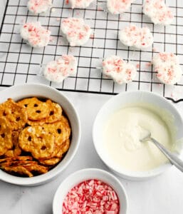 White Chocolate Peppermint Pretzel Crisps on Baking Rack with Bowls of Pretzel Crisps, Melted White Chocolate, and Crushed Peppermint on the Side