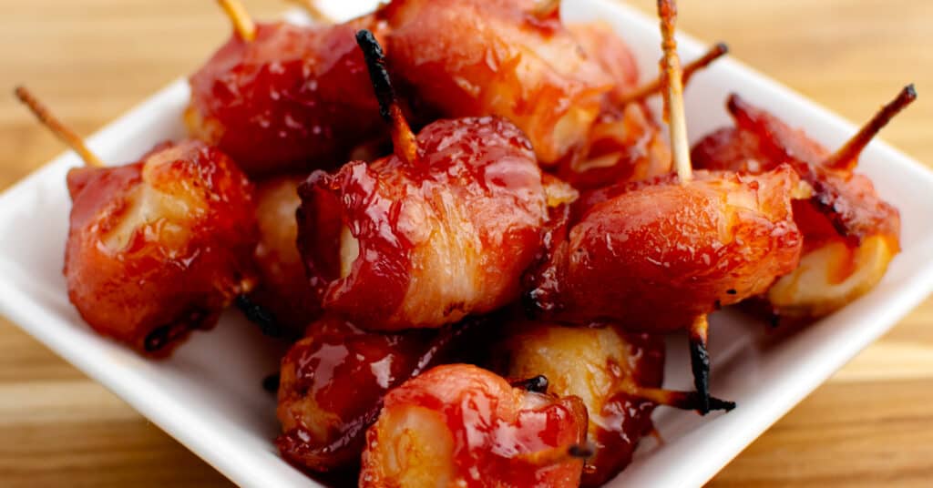 Bacon Wrapped Water Chestnuts Secured with Toothpicks in Square Bowl on Wooden Surface