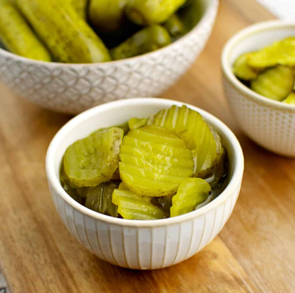 3 Kinds of Pickles in Bowls on Wooden Surface - Hamburger Dill, Bread and Butter, and Baby Dill Pickles