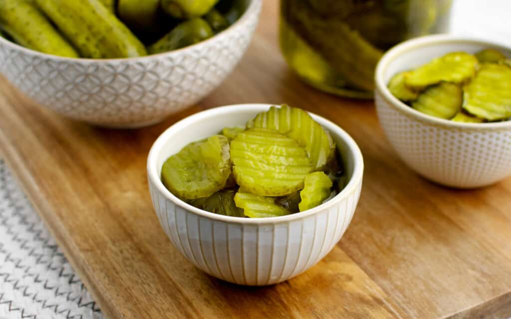 Hamburger Dill Pickles in a Bowl with Other Bowls of Pickles on Wooden Surface