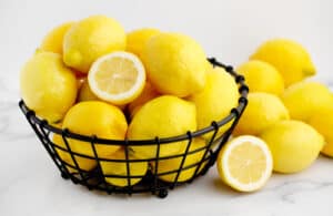 Black Wire Bowl with Lemons and Lemons on White Surface with Lemon Cut Open