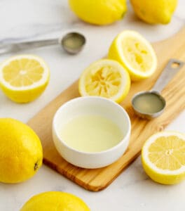 Small Bowl and Tablespoon of Lemon Juice on Wooden Cutting Board with Slices Lemons
