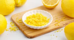 Lemon Zest in White Bowl on Cutting Board with Lemons on White Marble Surface