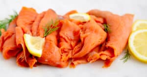 Cold Smoked Salmon Slices with Lemon and Herbs on White Surface