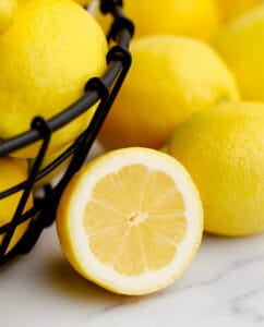Black Wire Bowl of Lemons with Half Lemon on Marble Surface