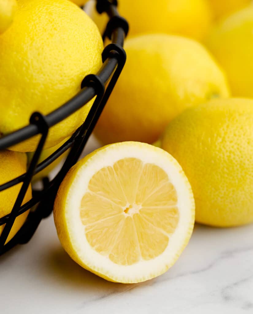 Black Wire Bowl of Lemons with Half Lemon on Marble Surface