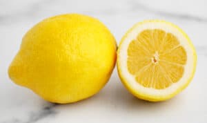 Whole Lemon and Half Lemon on White Marble Surface