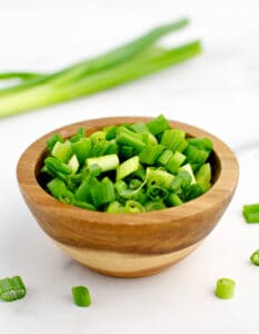 Chopped Green Onions in Wooden Bowl with Whole Green Onions in the Background