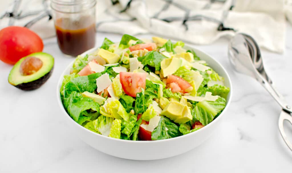 Avocado Tomato Romaine Salad in Bowl with Towel and Dressing Behind