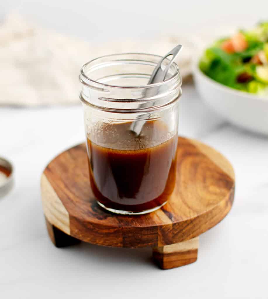 Dijon Balsamic Vinaigrette on Wooden Coaster with Salad in Background