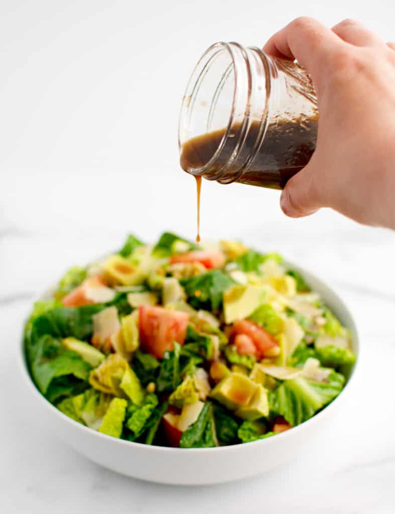 Pouring Dressing from Mason Jar onto Salad in White Bowl