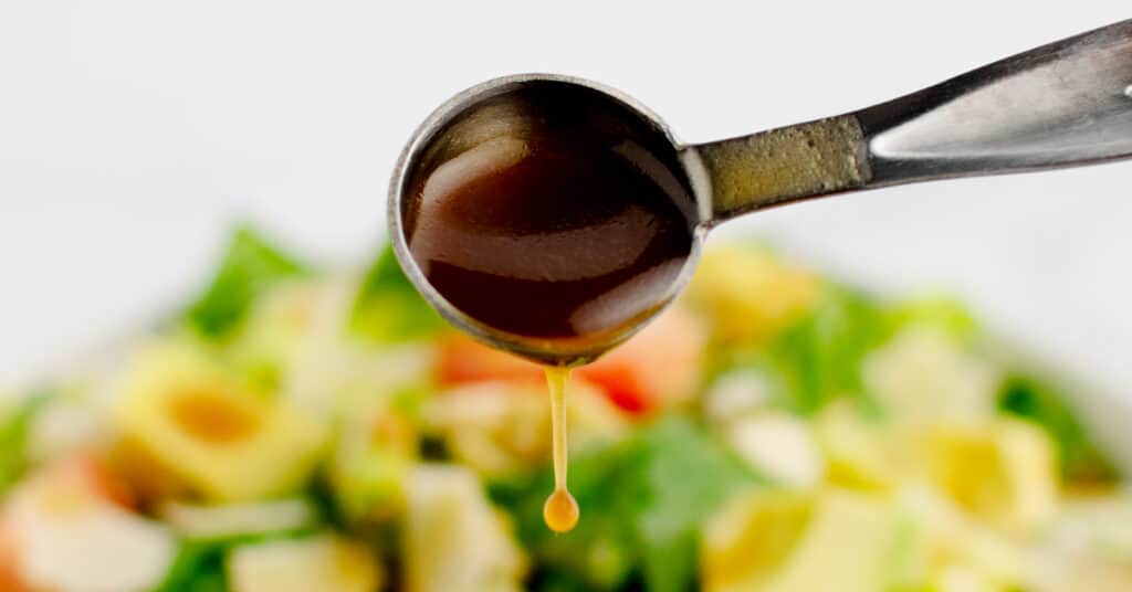 Dijon Balsamic Vinaigrette on Spoon Pouring on to Green Salad in Bowl