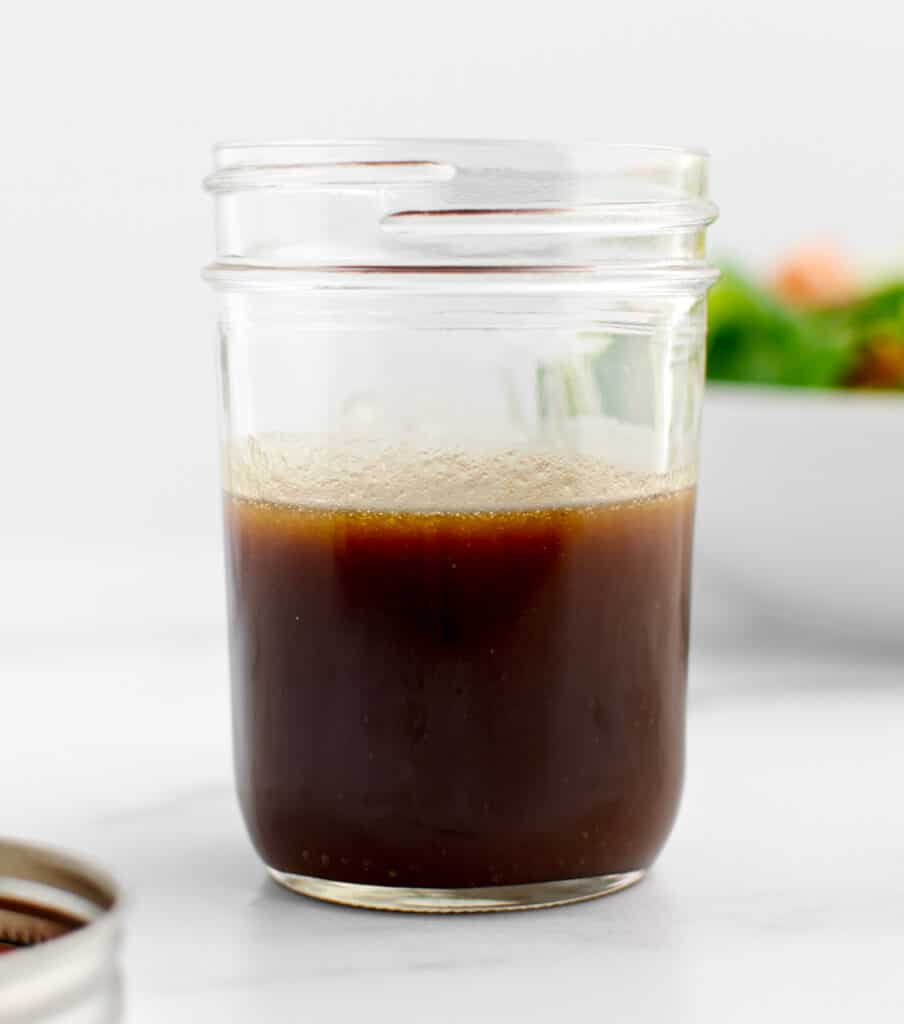 Dijon Balsamic Vinaigrette in Mason Jar with Lid Next to It and Salad Behind