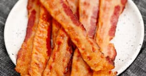 Cooked Bacon Piled on a Plate with Grey Napkin